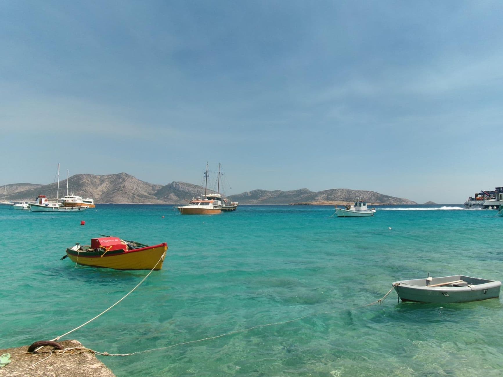 Boats on the turquoise water of Milos under a clear summer sky