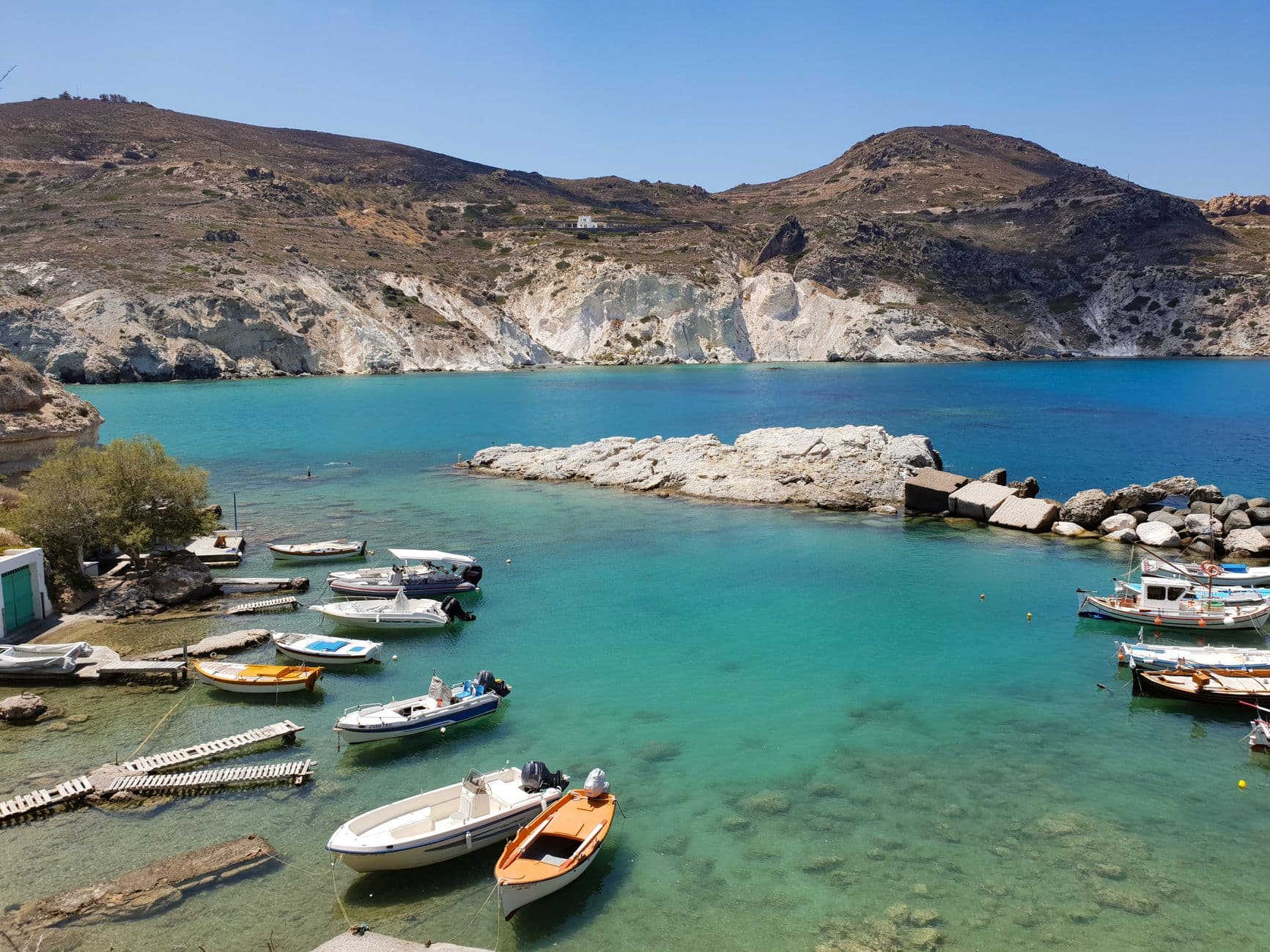 Bay on Milos with clear water, small boats and rocky cliffs