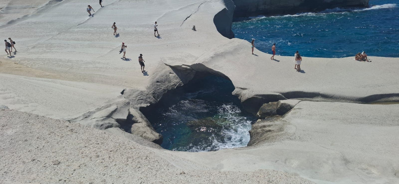 Visitantes en torno al pozo de la cueva marina en el paisaje lunar blanco de Sarakiniko, Milos