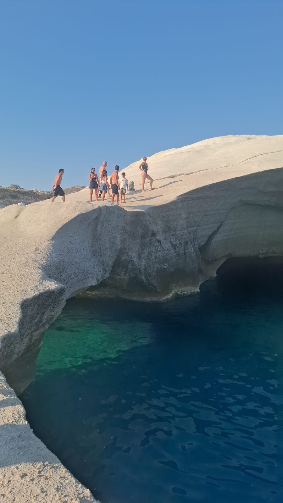 Family standing above the turquoise sea cave at Sarakiniko beach, Milos